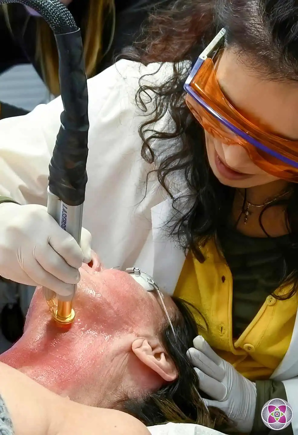 A medical professional wearing orange laser safety goggles performs a targeted laser vein removal treatment on a patient's neck area in a clinical setting.